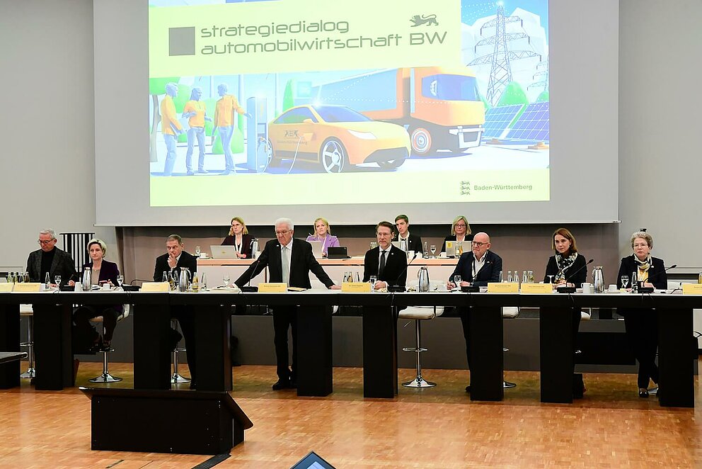 Ministerpräsident Winfried Kretschmann eröffnet das Top-Level-Meeting auf dem Strategiedialog Automobilwirtschaft BW. Er ist umgeben von anderen wichtigen Vertreter:innen der Industrie.